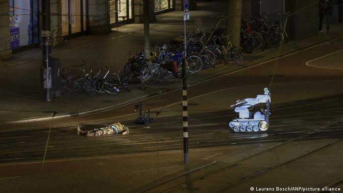 Mężczyzna w kamuflażu leży obok policyjnego robota na ulicy