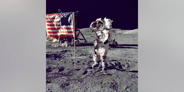 Astronauta Eugeniusz A.  Cernan, dowódca Apollo 17, pozdrawia amerykańską flagę na powierzchni Księżyca podczas niedawnej misji lądowania na Księżycu (EVA).  jednostka księżycowa "Pretendenta" W lewym tle znajduje się za flagą, a łaziki księżycowe (LRV) są również w tle.  Cernan był ostatnim człowiekiem, który chodził po Księżycu po ukończeniu programu Apollo. 